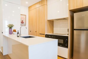 A modern kitchen with white cabinetry, a stainless steel refrigerator, a built-in oven, and a sink with a vase of flowers. - Inner South Stay, Minutes to Manuka and Foreshore (Griffith)