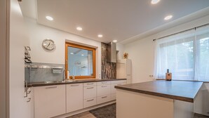 A modern kitchen with white cabinetry, a built-in oven, a sink, and a window with sheer curtains. - Modern holiday apartment with terrace and garden (Mittersill)