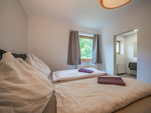 Une chambre à coucher avec un lit, une fenêtre avec des rideaux, un radiateur et une salle de bain visible à travers une porte ouverte.