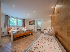 A bedroom with two beds, a window with curtains, a radiator, and a wooden headboard.