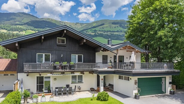 A two-story house with a balcony, a garage, and a well-maintained lawn. - Modern holiday apartment with terrace and garden (Mittersill)