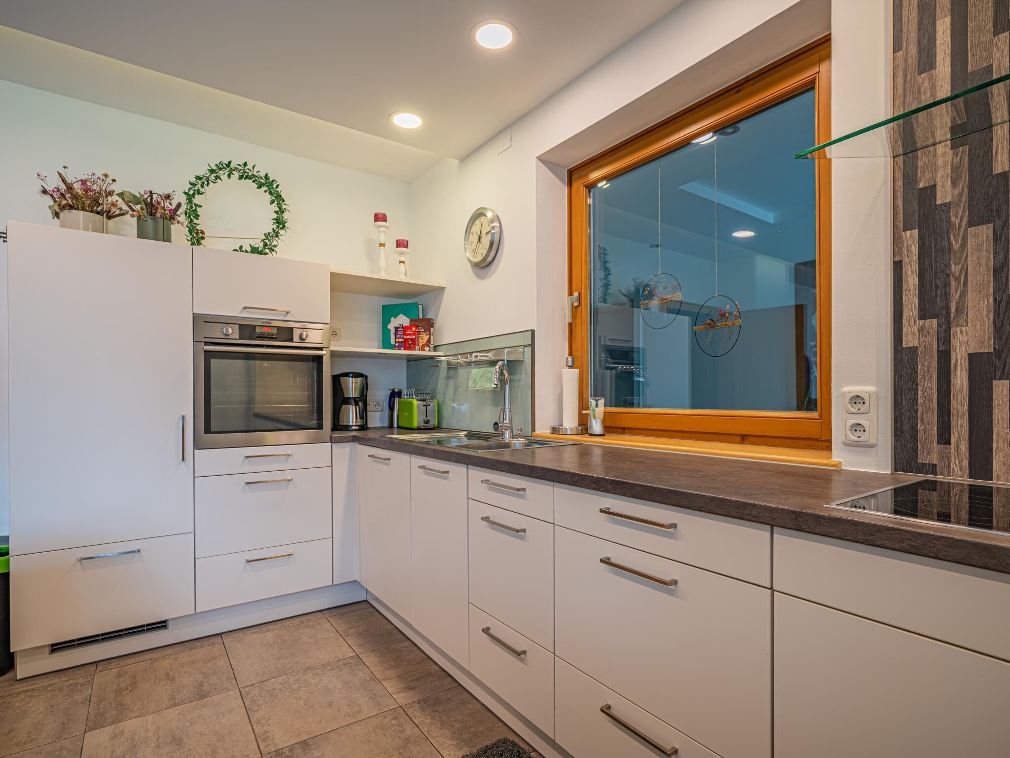 Una cocina moderna con armarios blancos, horno integrado, cafetera y ventana con vistas.