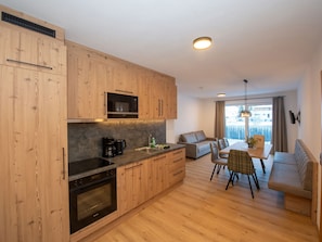 A modern kitchen with wooden cabinets, a built-in microwave, and a dining area with a sofa and table. - Apartment with sauna directly on the slope (Hinterglemm)