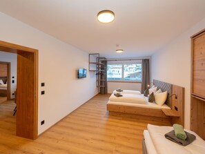 A modern hotel room with a wooden floor, two beds, a TV, a window with a view, and a wooden wardrobe. - Apartment with sauna directly on the slope (Hinterglemm)