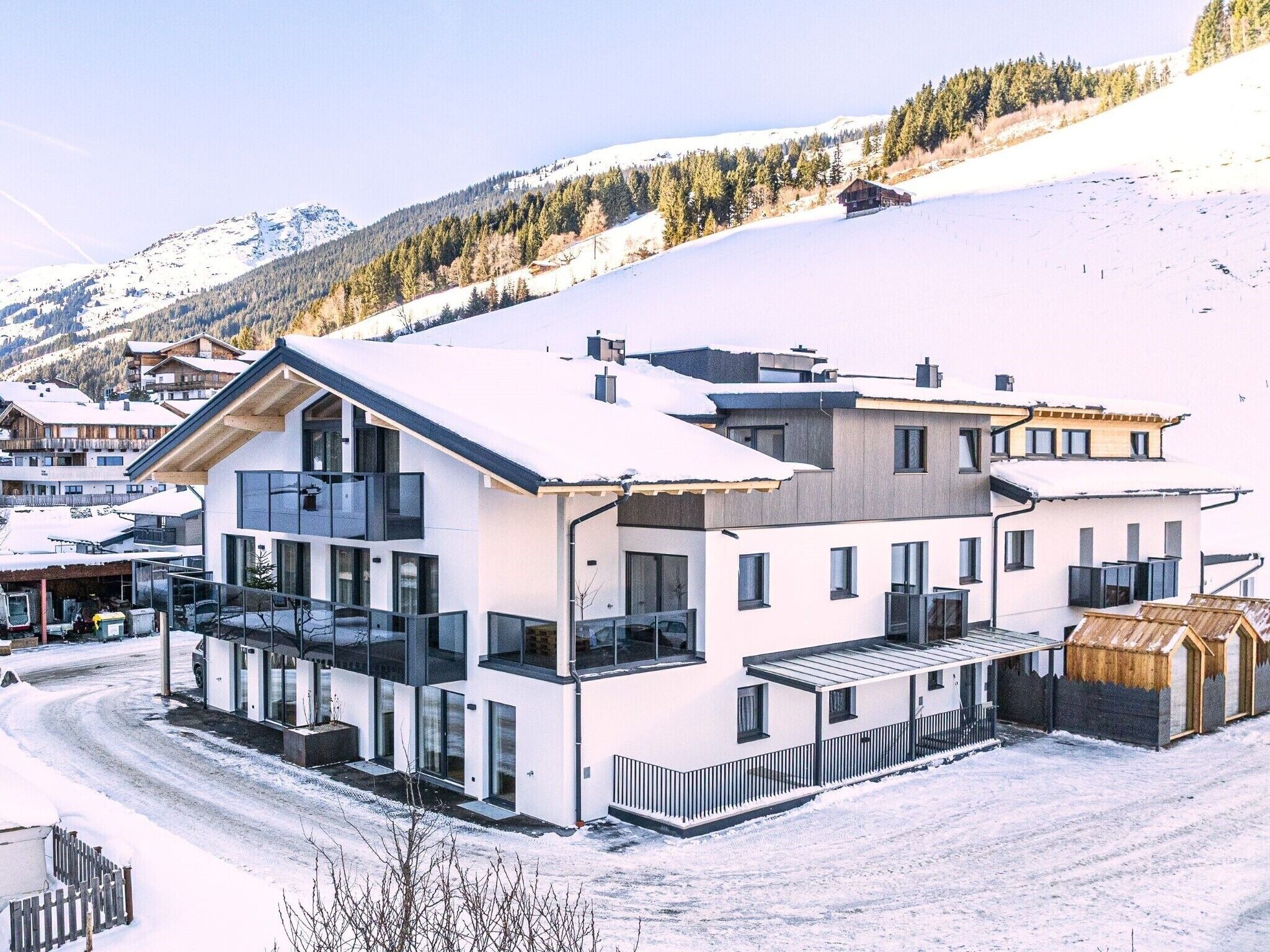 Ein modernes, mehrstöckiges Gebäude mit großen Fenstern, einem Balkon und einer Skipiste im Hintergrund.