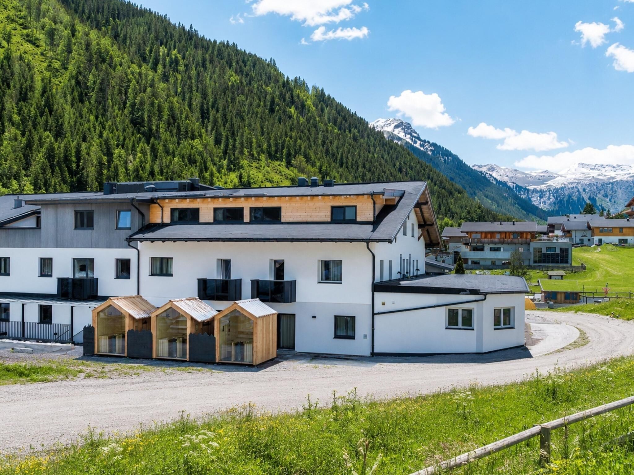 Ein modernes Hotel mit mehreren Zimmern, einer überdachten Außenfläche und Blick auf eine gebirgige Landschaft.