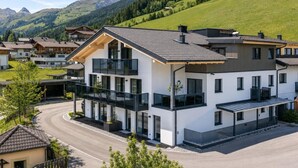 A modern multi-story building with a balcony, surrounded by a residential area and mountains. - Ski-in apartment with sauna in the house (Hinterglemm)