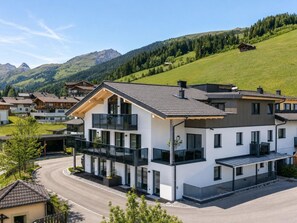 Ein modernes, mehrstöckiges Gebäude mit Balkon, umgeben von einer Wohngegend und Bergen.