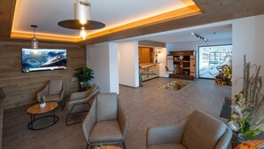 Ein modernes Wohnzimmer mit Flachbildfernseher, bequemen Sitzmöglichkeiten, einem Couchtisch und einem Glastisch.