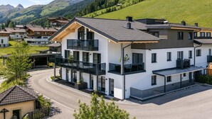 Ein modernes, zweistöckiges Gebäude mit großen Fenstern, einem Balkon und Blick auf einen grünen Hügelhang.