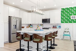 A modern kitchen with white cabinets, a stainless steel refrigerator, a microwave, and a bar area with stools.
