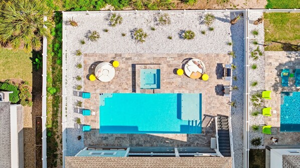 An aerial view of a pool area with a large pool, sun loungers, and a small table with chairs.