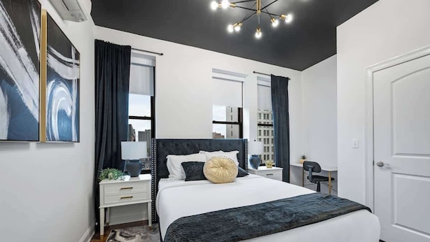 Een moderne slaapkamer met een groot bed, nachtkastjes, een spiegel en een deur.