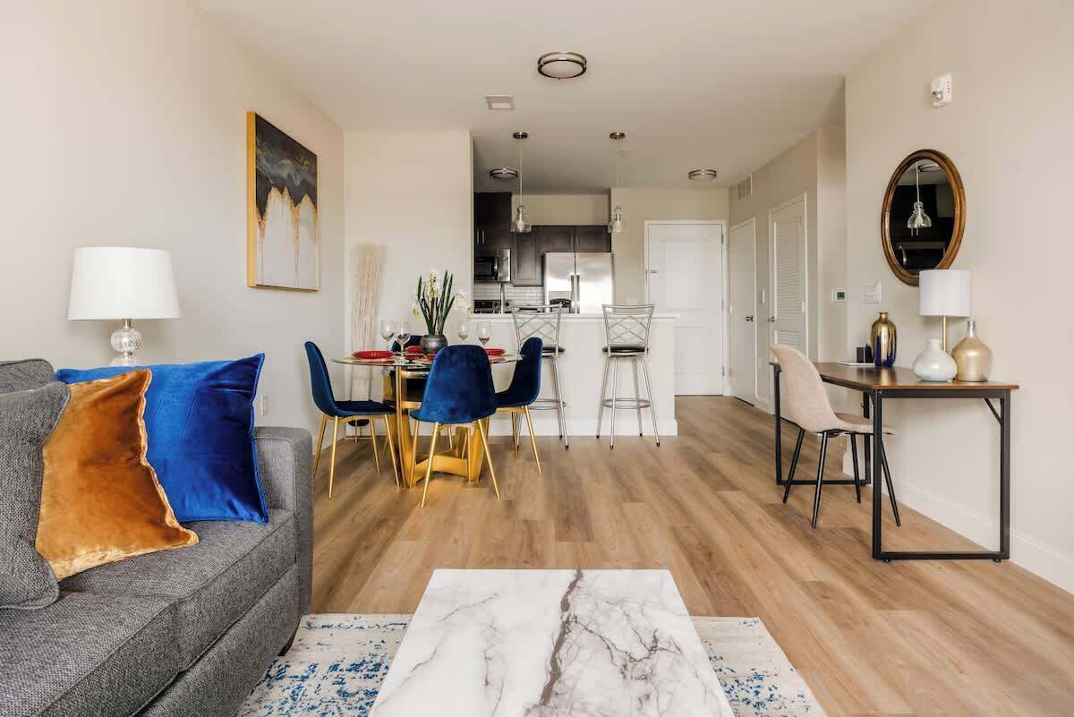 A modern living room with a sofa, a dining area with chairs, and a kitchen in the background.