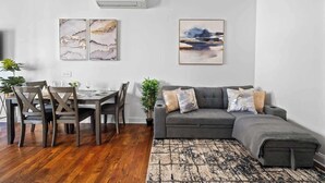 Ein modernes Wohnzimmer mit Essbereich, grauem Sofa, Holztisch und Kunstwerk an der Wand.