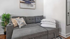Ein graues Ecksofa mit Kissen, einer Topfpflanze und einem gerahmten abstrakten Gemälde an der Wand.