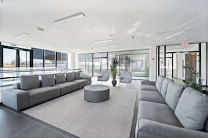 Un hall d’entrée moderne avec un canapé d’angle gris, une table basse ronde et une grande plante en pot.
