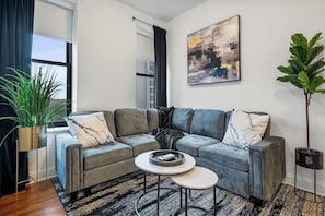Ein modernes Wohnzimmer mit einem grauen Ecksofa, einem Couchtisch, einer großen Kühlpflanze und einem Gemälde an der Wand.
