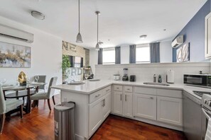 Eine moderne Küche mit weißen Schränken, einem Essbereich mit Tisch und Stühlen sowie einem großen Fenster mit Vorhängen.