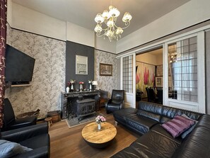 Ein modernes Wohnzimmer mit Kamin, Ledersofas, einem Couchtisch und einer Kristallleuchter.