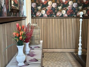 Ein Empfangsbereich mit Wandverkleidung aus Holz, blumigem Wandpapier, einer weißen Vase mit roten Blumen und einem gemusterten Teppich.