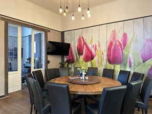 Ein Essbereich mit einem runden Holztisch, umgeben von Stühlen, einem an der Wand befestigten Flachbildfernseher und einem großen Blumenfries.