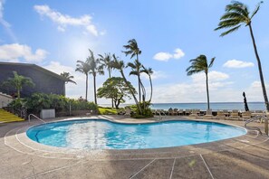 Ein Pool mit Liegestühlen und Palmen, ein Gebäude mit Treppe und Blick auf den Ozean.