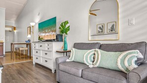 Ein Wohnzimmer mit grauem Sofa, Couchtisch, Fernseher und einem großen Gemälde mit Strandmotiv.