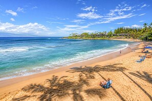 Ein Strand mit klarem, blauem Wasser, Palmen und einem Resort mit mehreren Gebäuden.