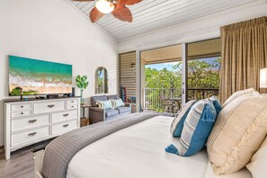 A bedroom with a large bed, a dresser, a television, and a view of the outdoors through a sliding door.