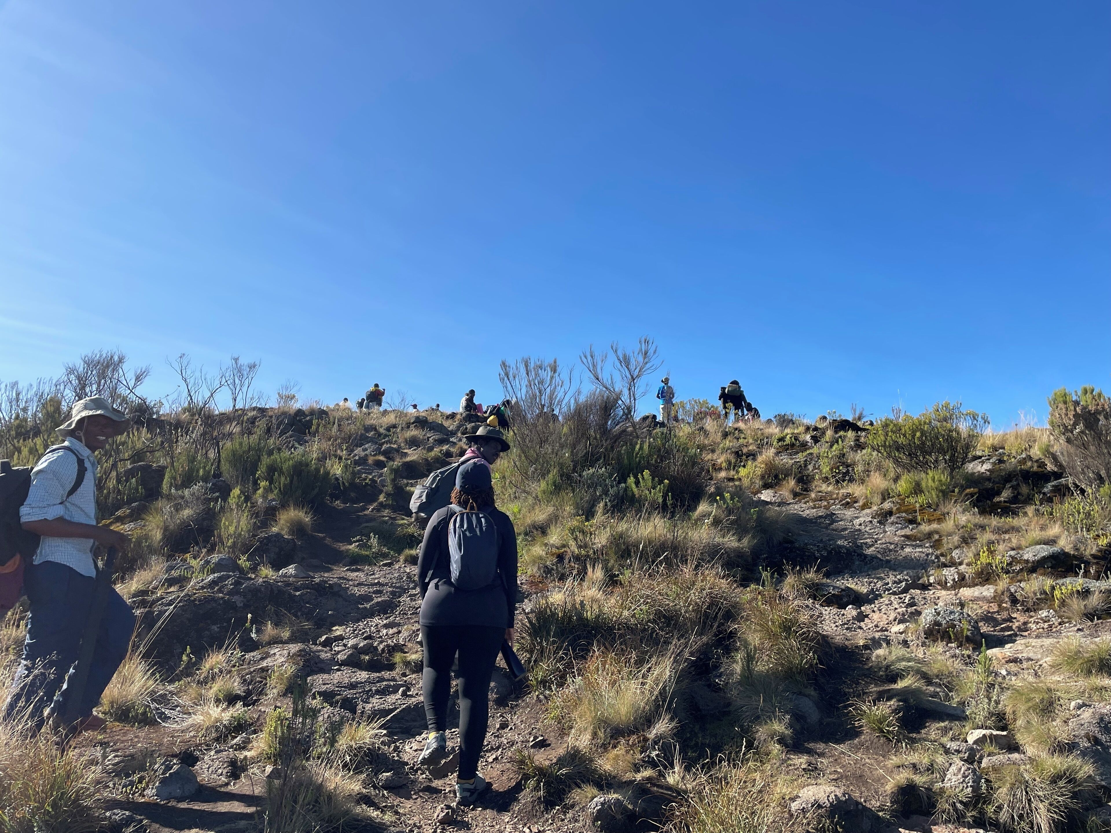 A group of people hiking on a rocky trail surrounded by sparse vegetation.