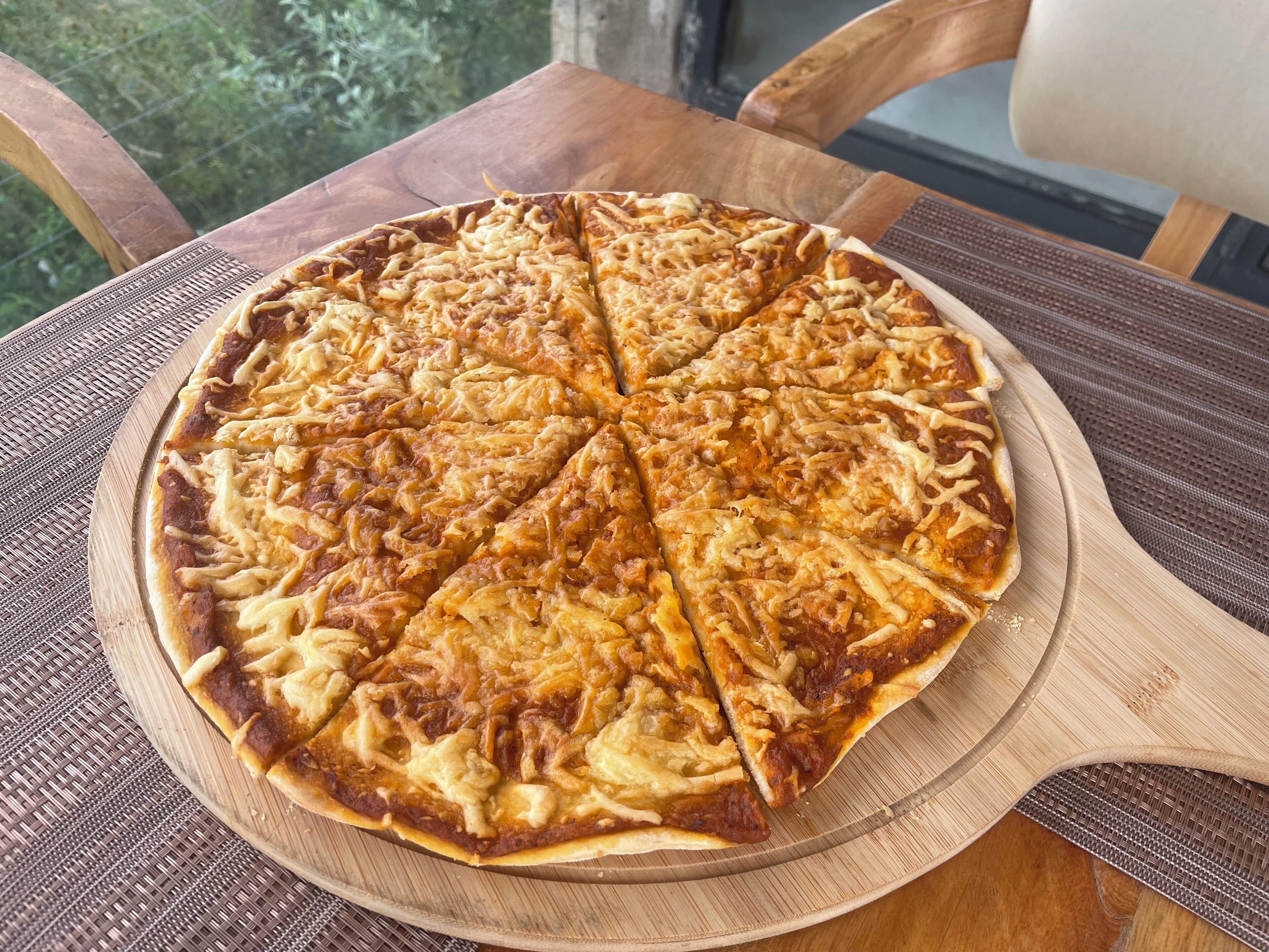 Una pizza sobre una tabla de madera en una mesa con una silla.