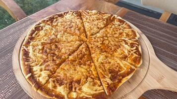 Una pizza sobre una tabla de madera en una mesa con una silla.