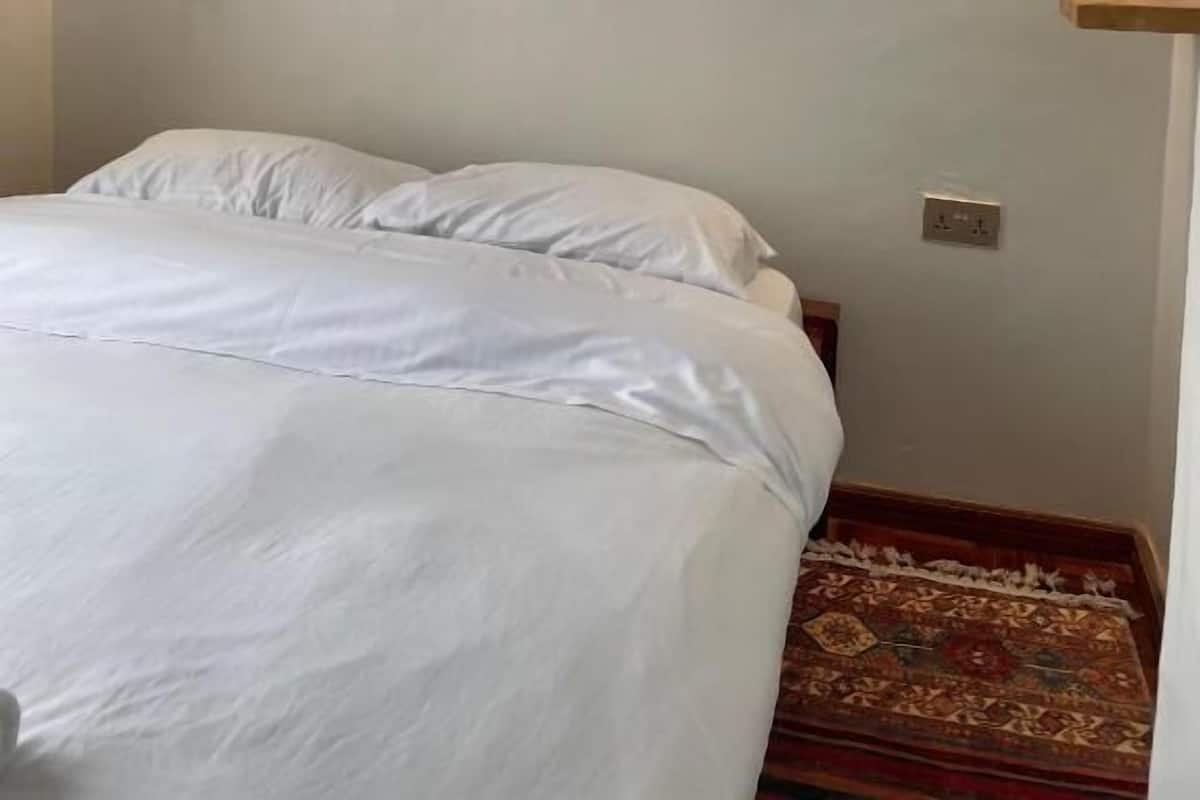 Un dormitorio con una cama, dos lámparas de pared, un estante de madera y una alfombra estampada.