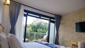 A hotel room with a bed, a TV, a balcony with a chair, and a brick wall. - Idan Barn Suites and Cafè (Naro Moru)