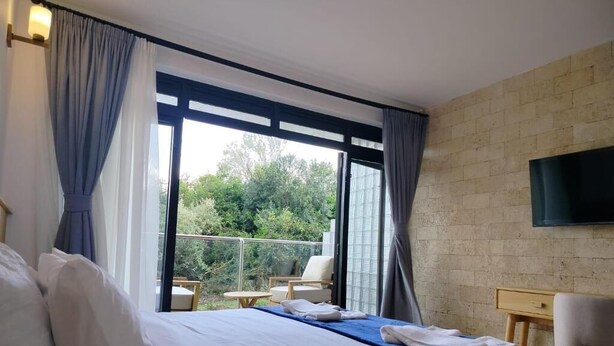 A hotel room with a bed, a TV, a balcony with chairs, and a brick wall. - Idan Barn Suites and Cafè (Naro Moru)