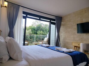 Una habitación de hotel con cama, televisión, balcón con sillas y pared de ladrillo.