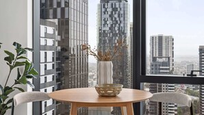 A modern room with a large window, a round table with two chairs, a vase with branches, and a potted plant.