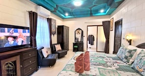 Une chambre à coucher comprenant une télévision, une armoire, un miroir et un lit recouvert d’une couvre-lit à motifs.