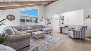 A spacious living area with a sofa, armchair, coffee table, and a large window providing a view of the outside. - Sand and Spa Retreat in Del Mar (Del Mar)