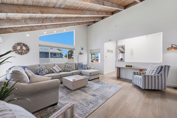 A spacious living area with a sofa, armchair, coffee table, and a large window providing a view of the outside.