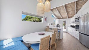 A modern kitchen with white cabinets, a stainless steel refrigerator, and a dining area with a round table and wicker chairs. - Sand and Spa Retreat in Del Mar (Del Mar)