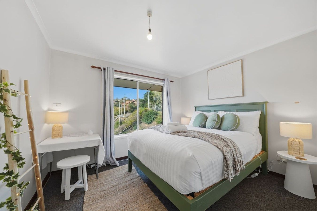 A bedroom with a bed, bedside tables, a desk, and a window with a view.