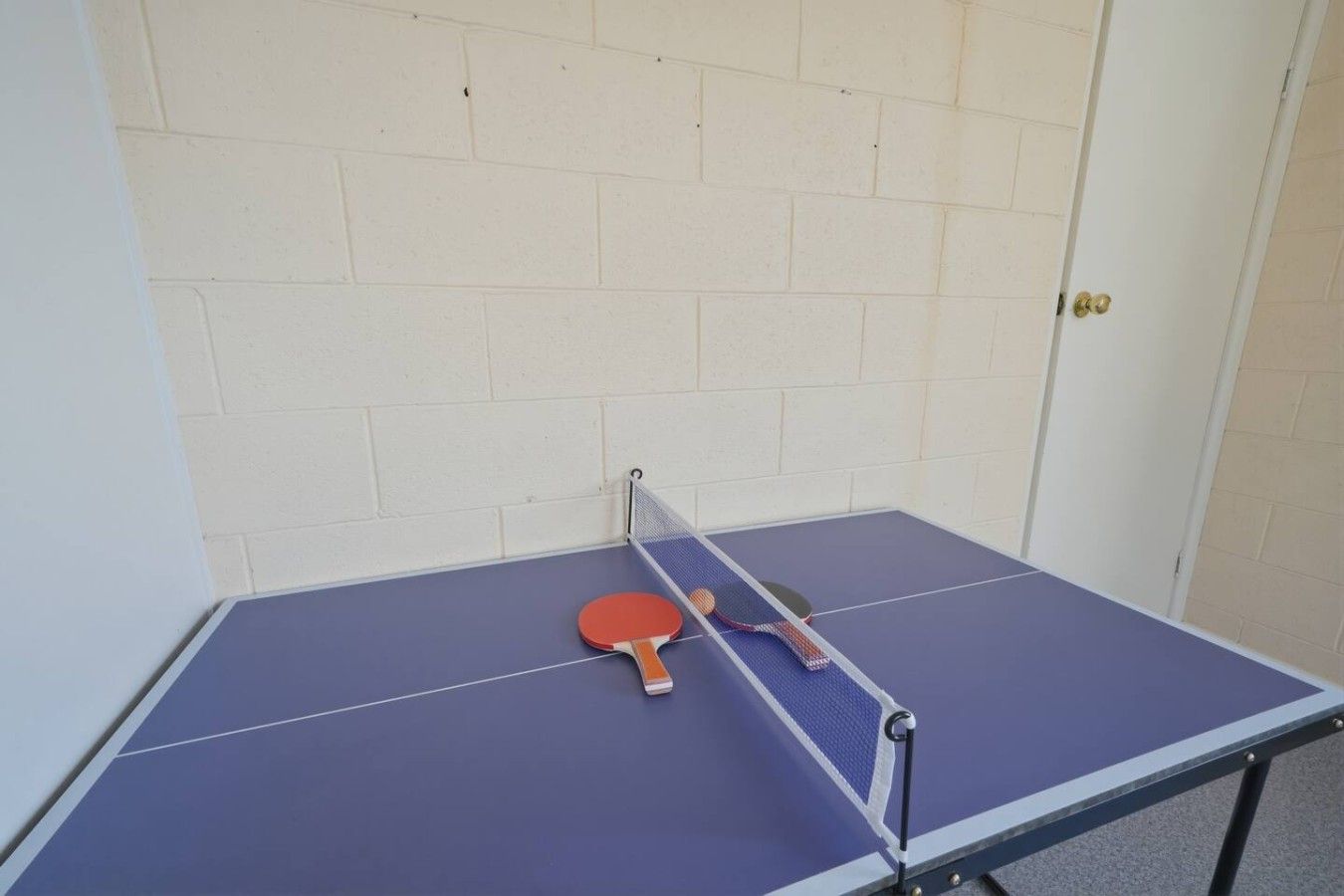 Ein Pingpongtisch mit Netz in der Mitte, einem roten Schläger und einer blauen Tischplatte.