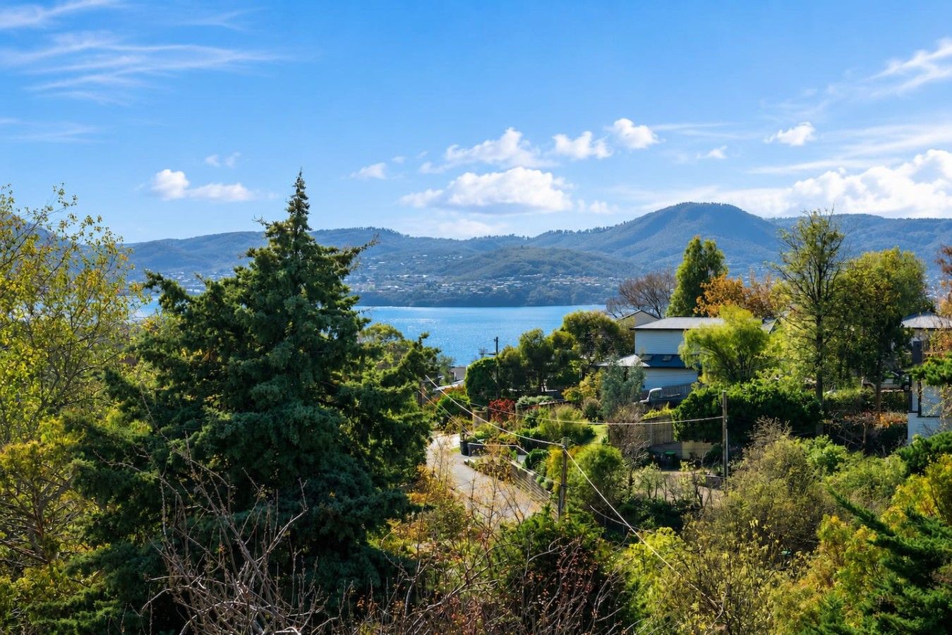A coastal landscape with a view of the sea, mountains in the distance, and a house surrounded by trees.