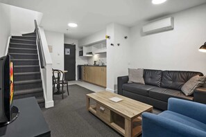Eine moderne Wohnung mit Treppe, einem Wohnzimmer mit Sofa und Sesseln, einer Küchenzeile und einem Esstisch.