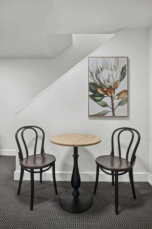 A room with a round table and two chairs, a framed botanical print on the wall, and a sloped ceiling. - City Centre - Little Bourke Street - 1BD Apartment (Melbourne)