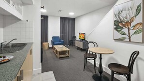 Una camera d'albergo compatta con angolo cottura, zona pranzo con tavolo e sedie, televisione e un quadro appeso al muro.
