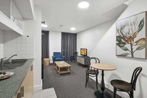 Ein kompaktes Hotelzimmer mit Küchenzeile, einem Essbereich mit Tisch und Stühlen, einem Fernseher und einem Bild an der Wand.