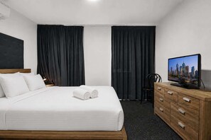 Ein Hotelzimmer mit Bett, Fernseher, einem Holzkapmierer und schwarzen Vorhängen.